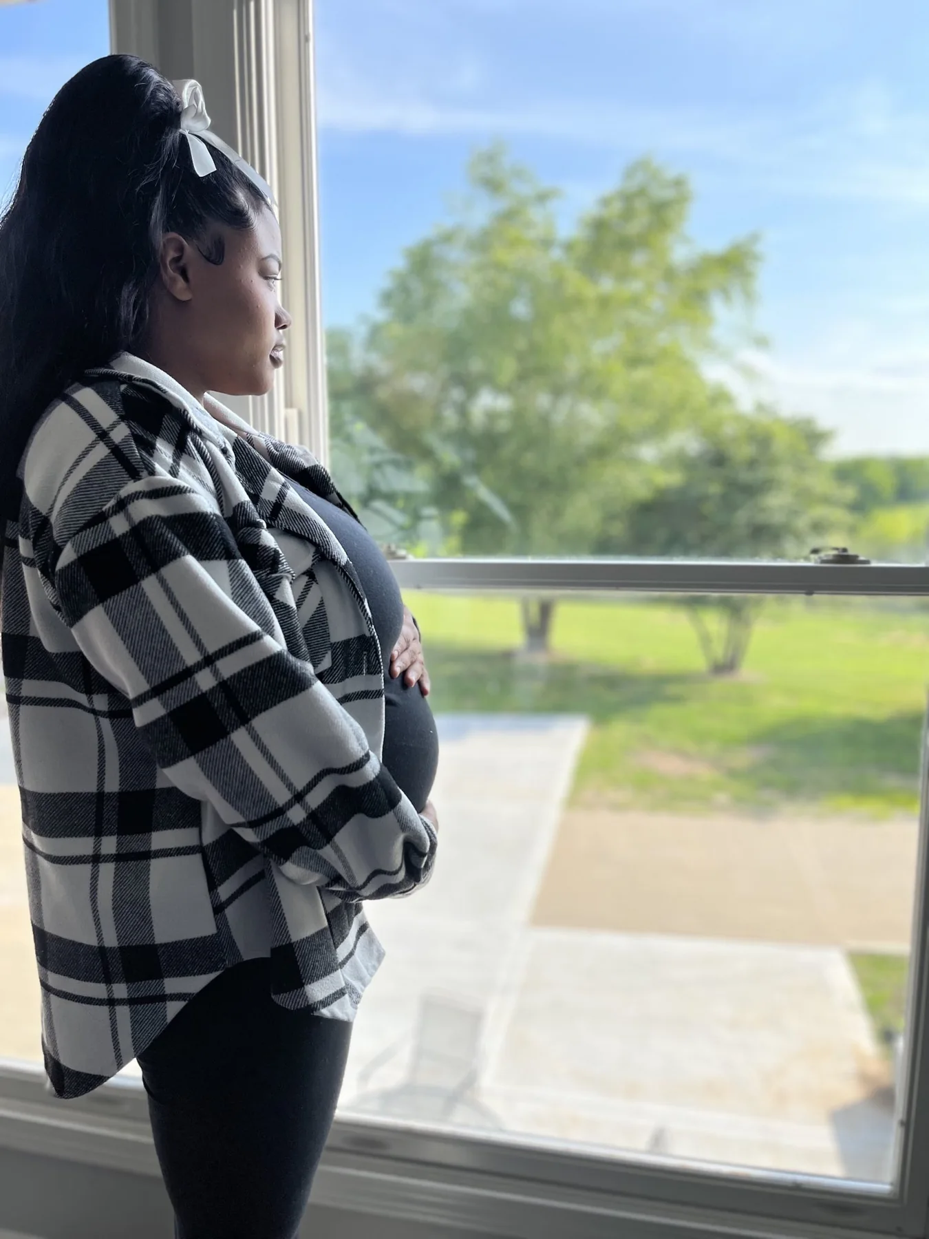 An expectant mother looking out over the grounds from a window inside the home